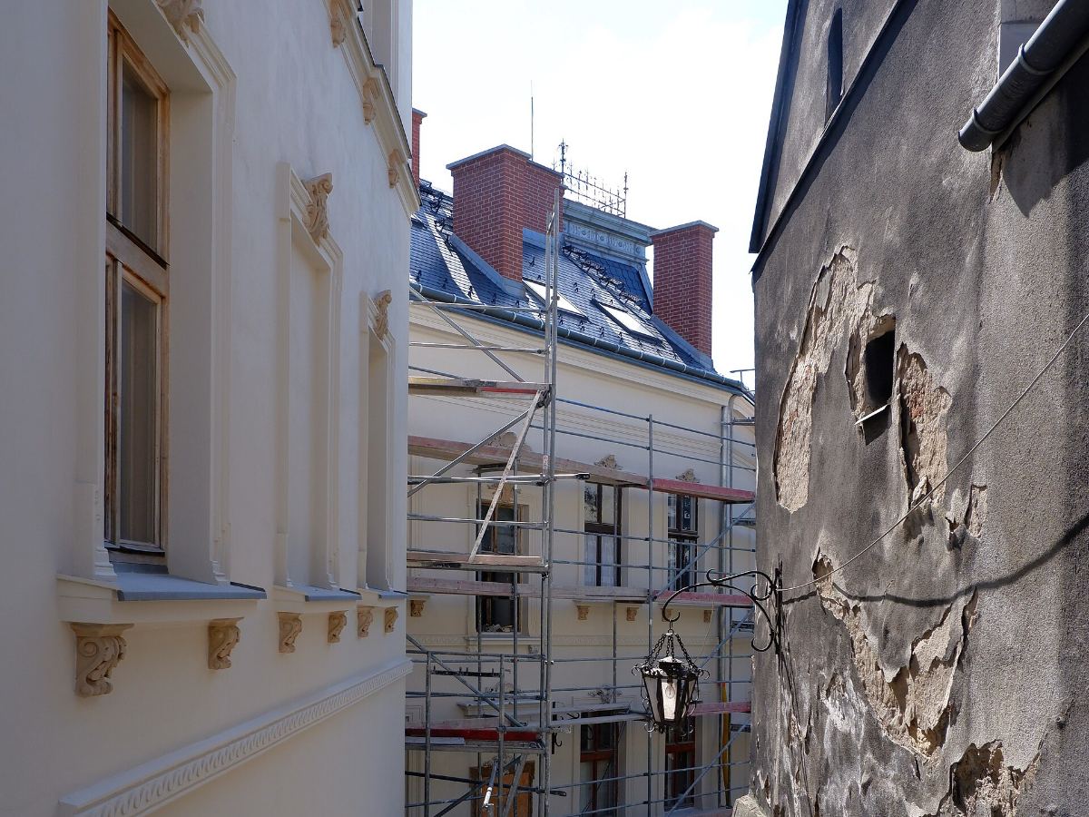 Ruelle en travaux, une façade déjà ravalée à gauche, un échafaudage au centre, un mur dont l’enduit est tombé à droite.