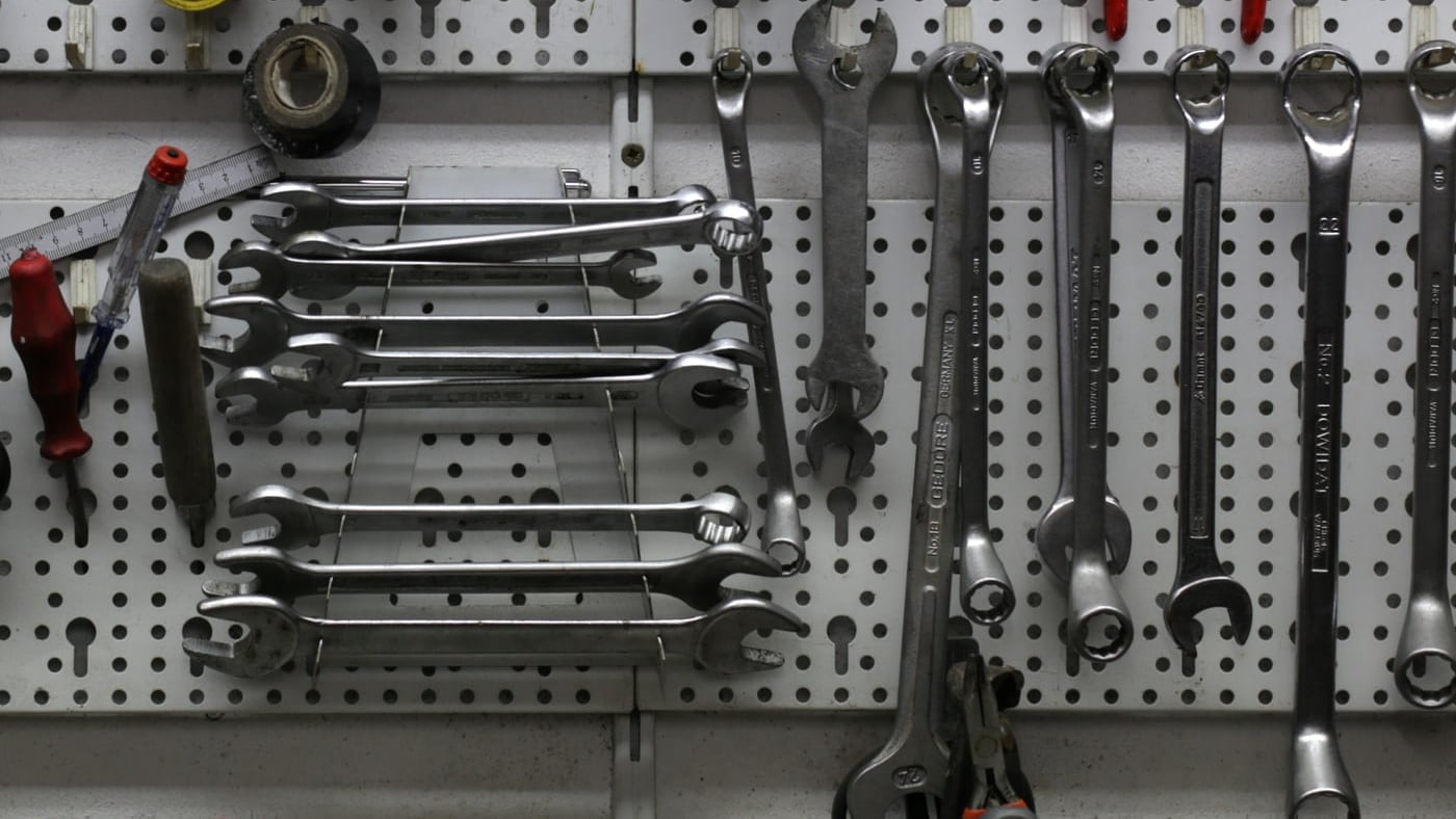 Panneau perforé d’atelier où sont rangées des clés plates chromées sur un râtelier, des clés mixtes suspendues et un mètre pliant.