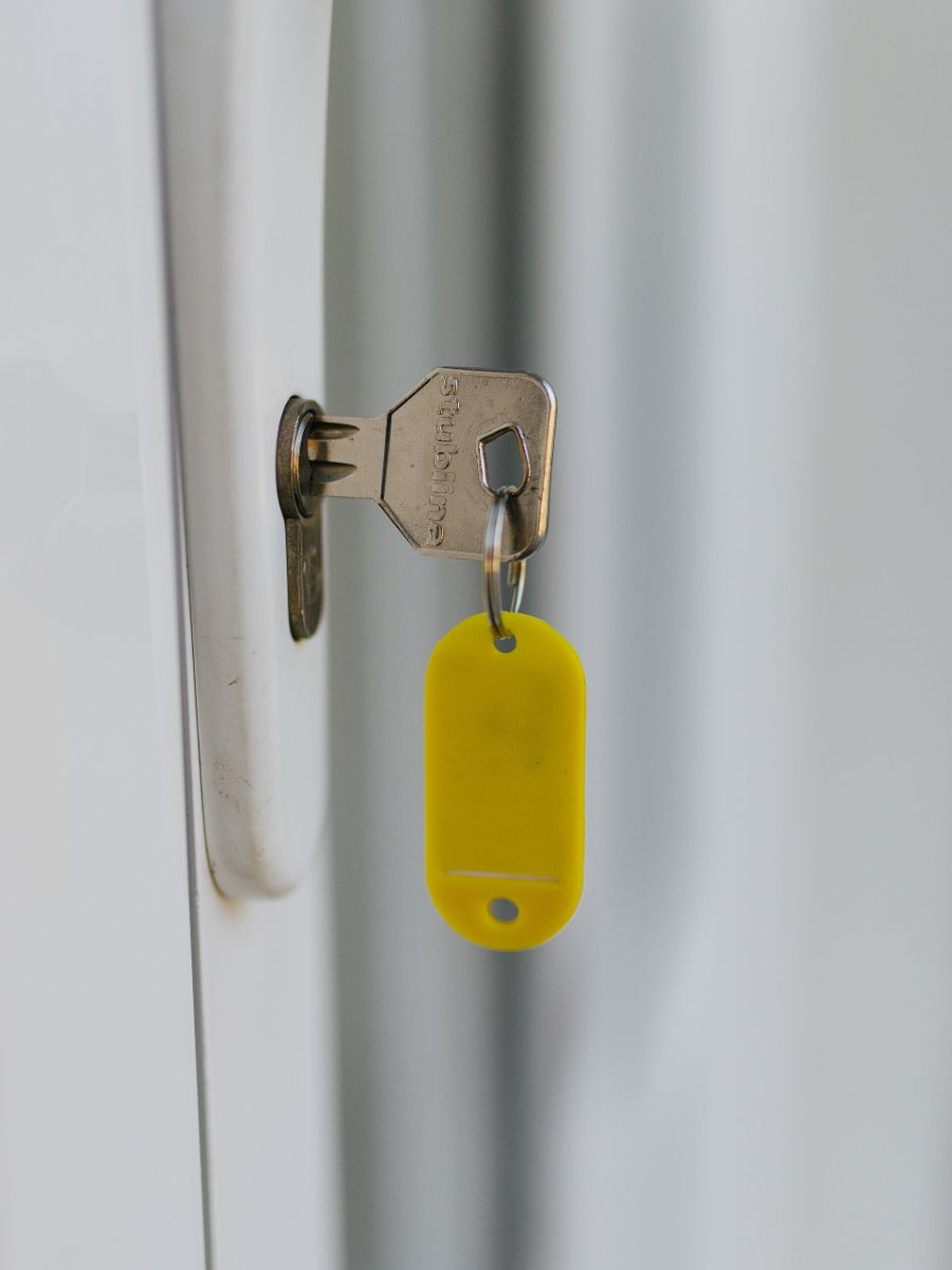Une clé avec son étiquette jaune, laissée sur la serrure d’une porte claire.