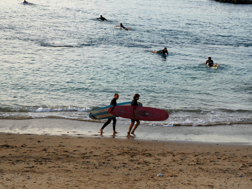 Deux surfeurs remontent la plage, planches sous le bras, en fin de journée