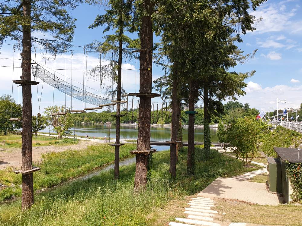 Parcours d'accrobranche au bord d'un plan d'eau, passerelles et filets tendus entre les pins