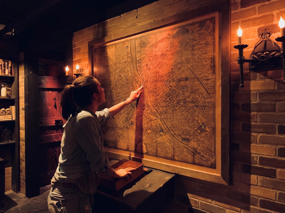Joueuse éclairée à la lampe désignant une vieille carte gravée accrochée au mur d'une pièce en briques