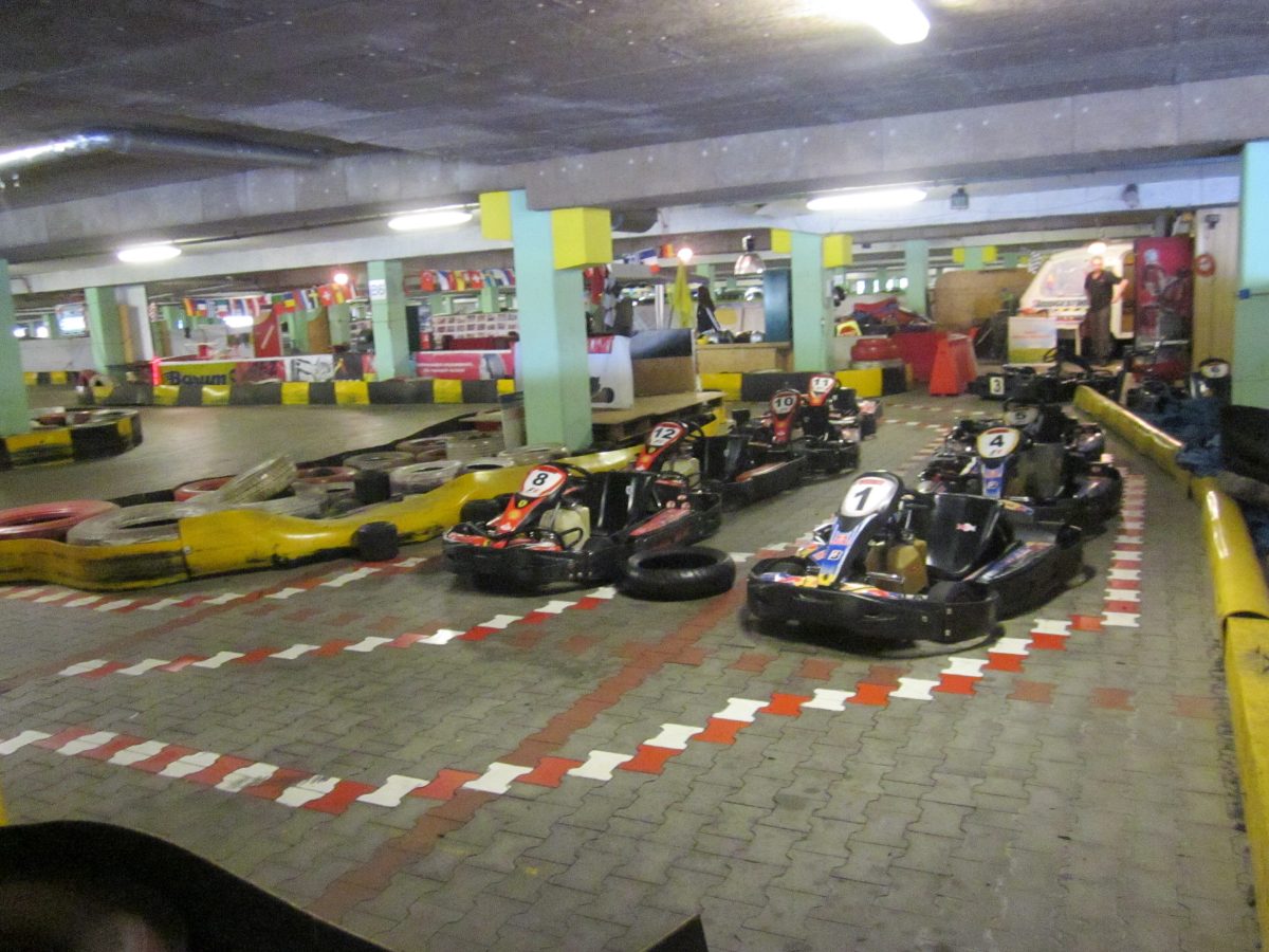 Karts alignés au départ d'une piste couverte, barrières jaunes et pneus de protection
