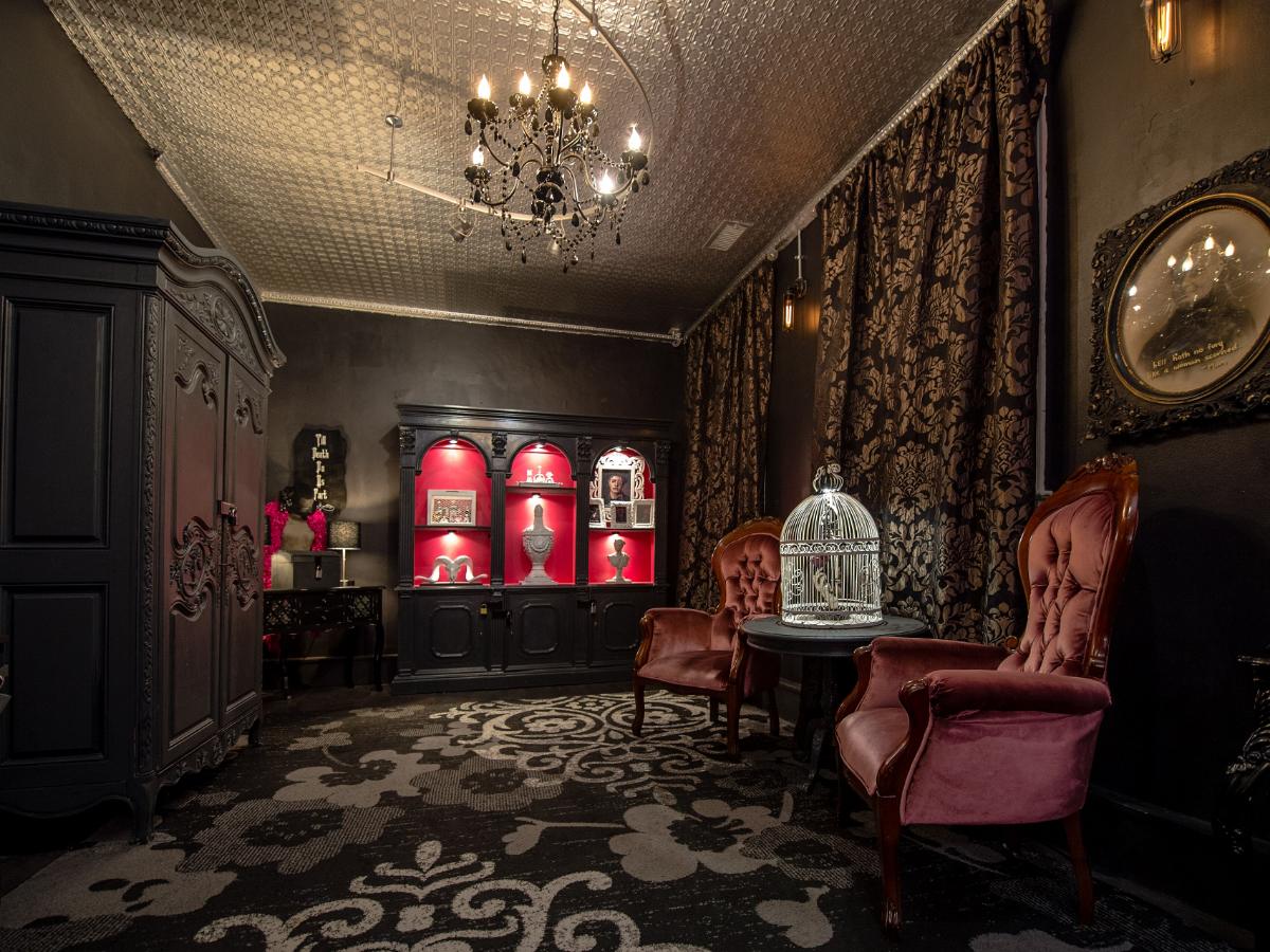 Salon d'un manoir ancien reconstitué, armoire sombre, fauteuils capitonnés et vitrine éclairée en rouge