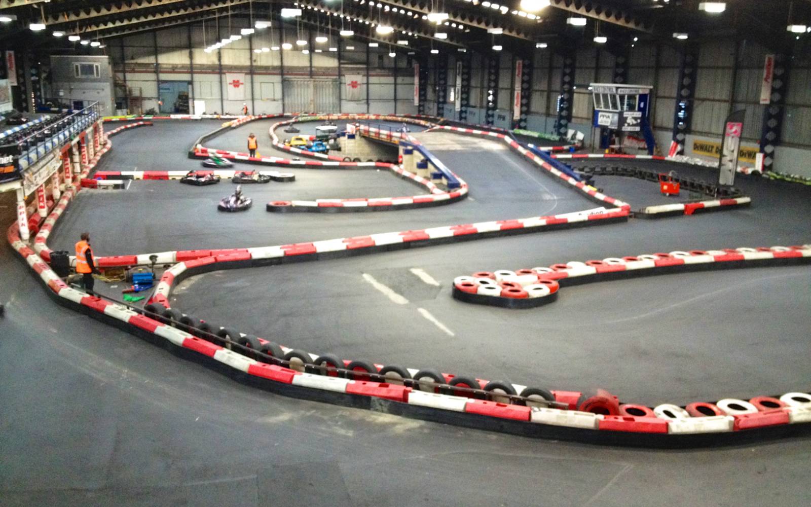 Grande halle couverte du parc, piste de mini-karting bordée de pneus rouges et blancs vue depuis les gradins