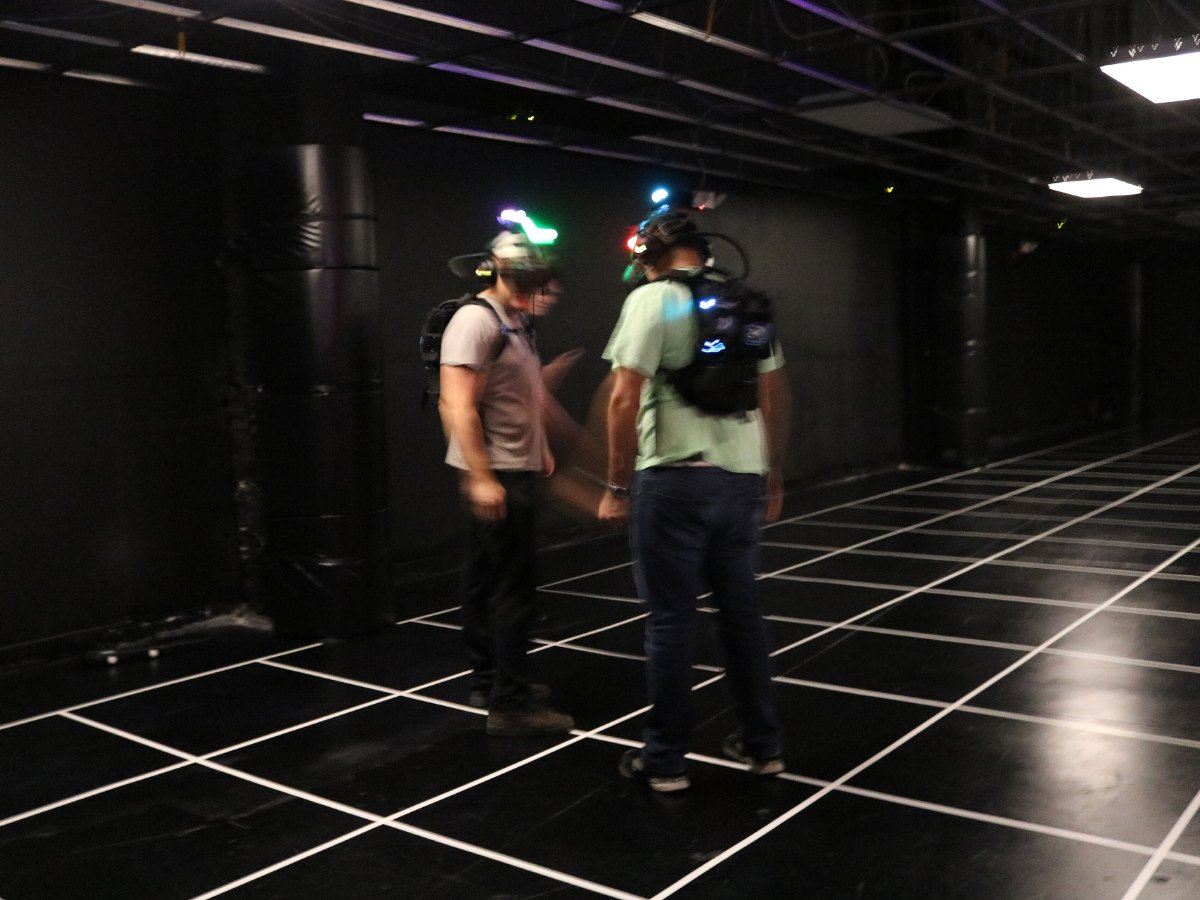 Deux joueurs équipés d'un casque et d'un sac à dos dans une salle sombre quadrillée de lignes lumineuses