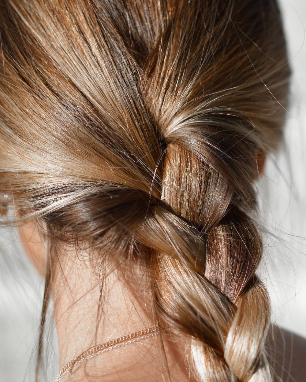Nuque avec une tresse basse, mèches claires travaillées au soleil