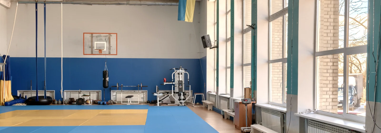 Salle de cours collectifs vide, tapis au sol, espaliers le long du mur et hautes fenêtres