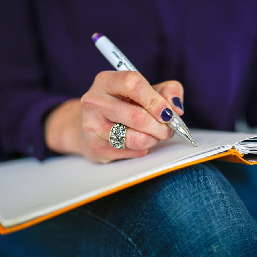 Main tenant un stylo au-dessus d'un carnet ouvert, lumière du jour
