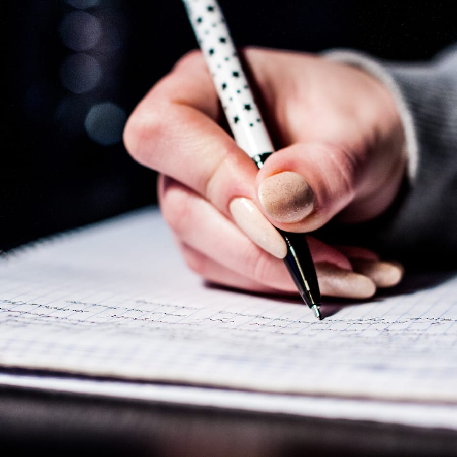 Main écrivant au stylo sur un cahier ligné, fond sombre