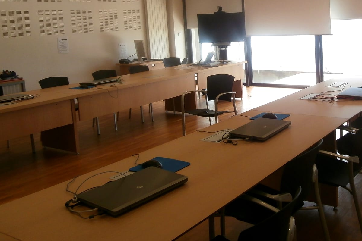Salle de cours du centre, longues tables en bois face à un écran, lumière venant des fenêtres