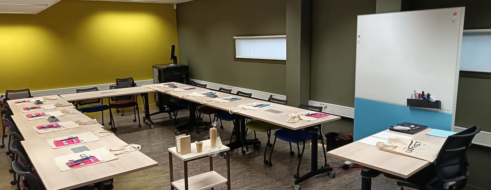 Salle de formation aux tables disposées en U, feuilles d'exercices posées à chaque place, tableau blanc au fond