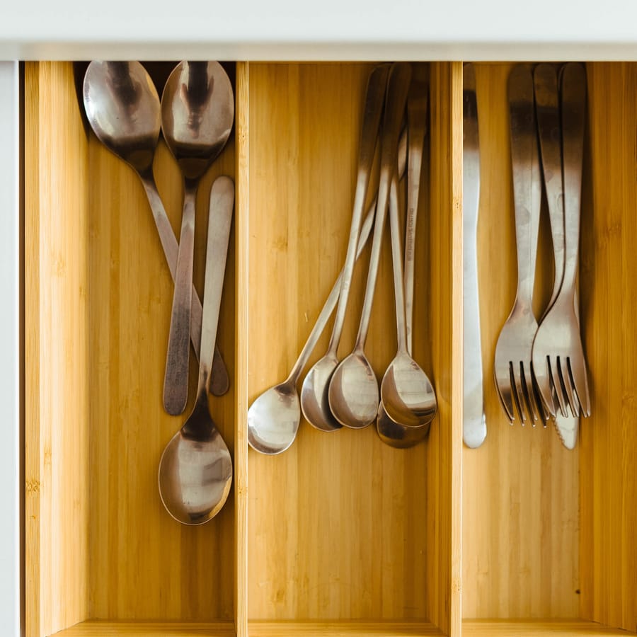 Tiroir de cuisine ouvert en pleine lumière, couverts rangés dans un casier en bois