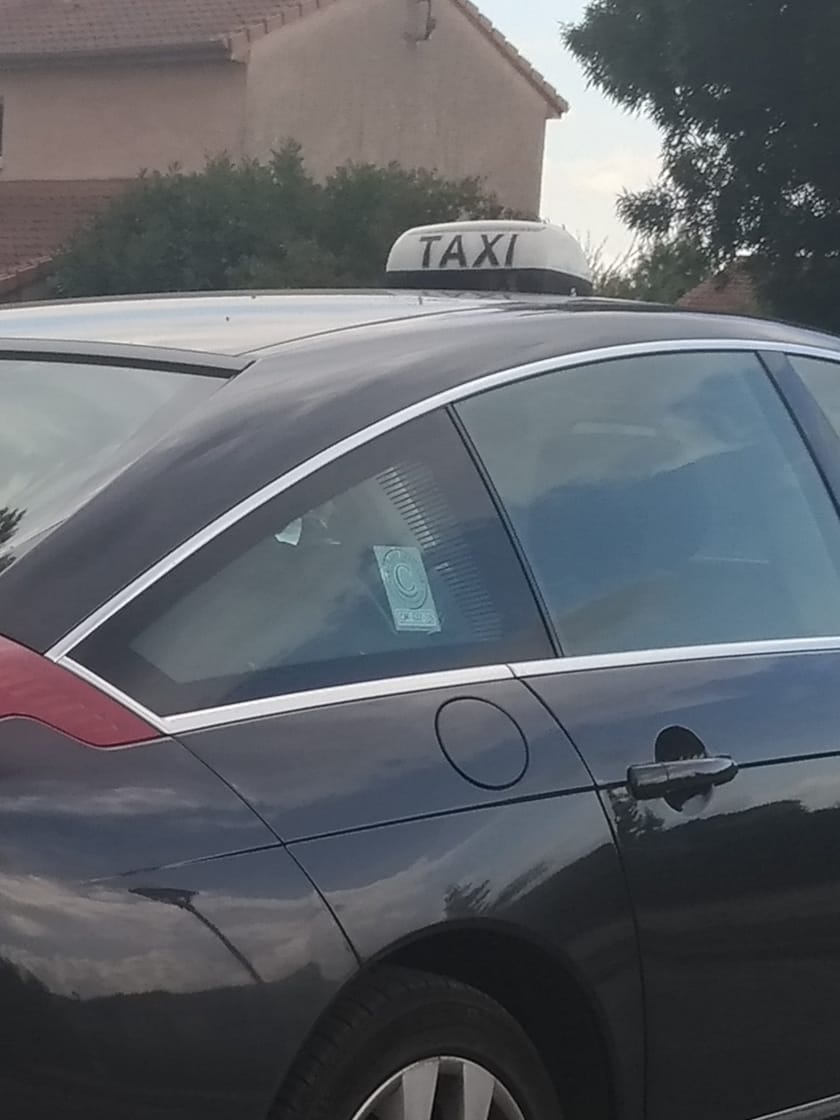Flanc d'une berline de taxi surmontée de son lumineux blanc marqué TAXI, en fin de journée