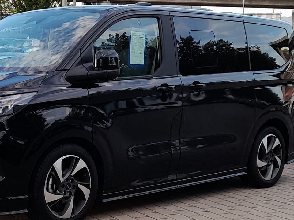 Van noir à huit places vu de profil sur un parking pavé