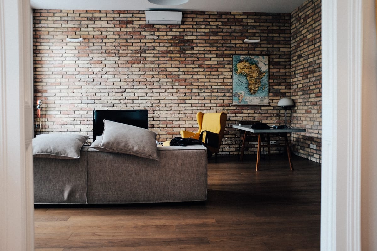 Séjour d'un deux pièces, mur de briques apparentes, canapé gris et parquet foncé