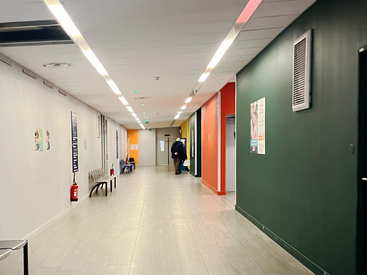 Couloir de consultations, sièges en enfilade et murs de couleur qui distinguent les ailes du bâtiment.