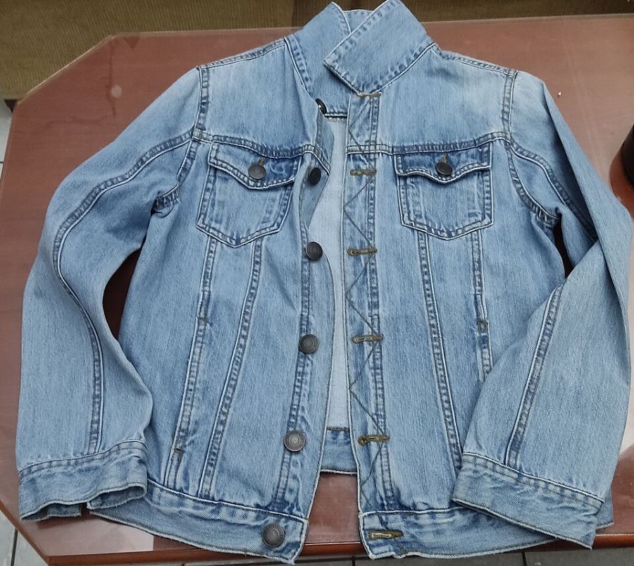 Veste en jean bleu clair posée à plat, boutons et poches visibles