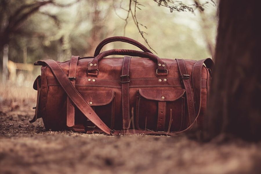 Sac de voyage en cuir brun à sangles, posé au sol