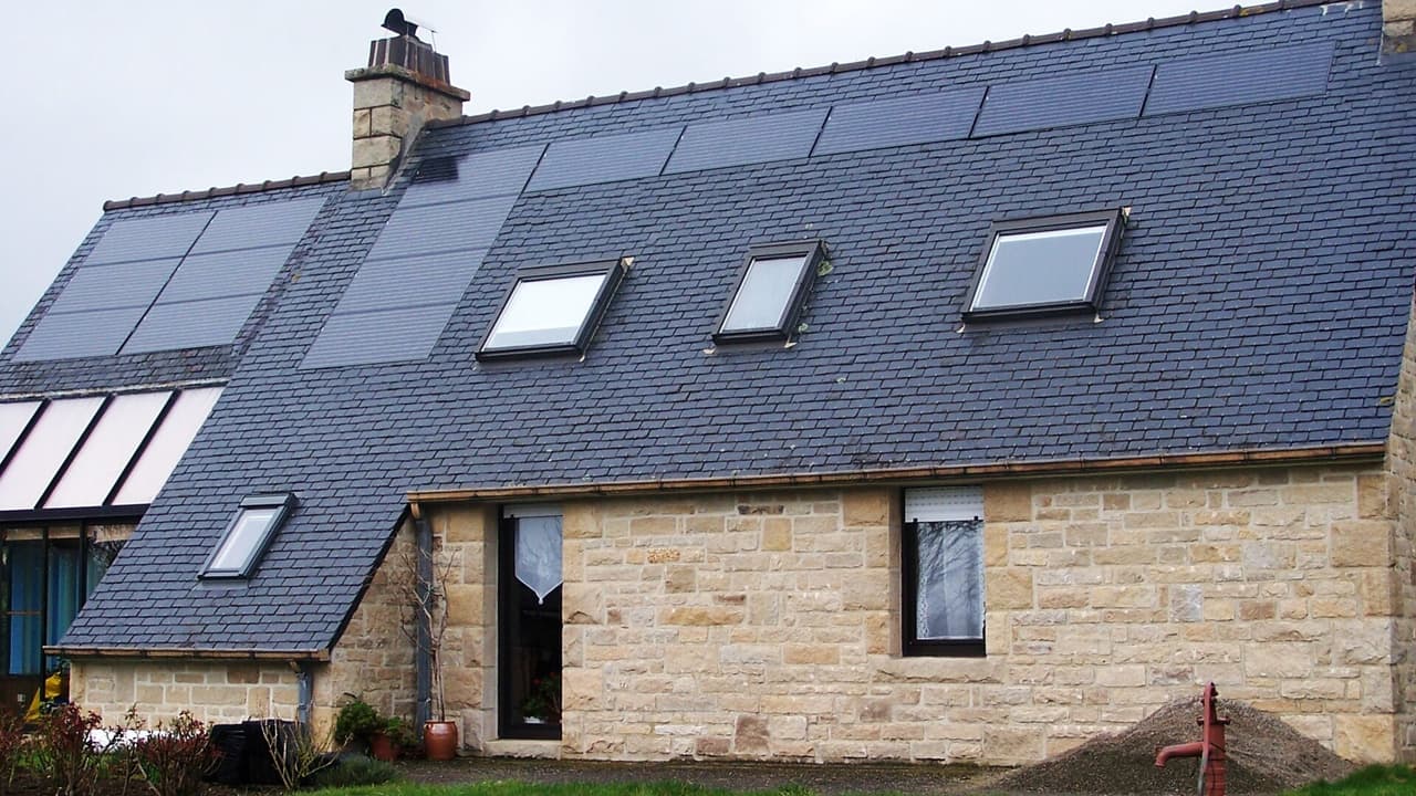 Maison en pierre couverte d'ardoises avec des modules photovoltaïques intégrés en toiture et des fenêtres de toit