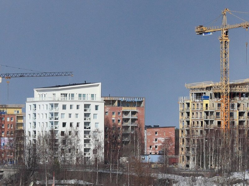 Chantier de logements collectifs, structure béton en élévation sous une grue à tour, immeubles déjà livrés à côté.