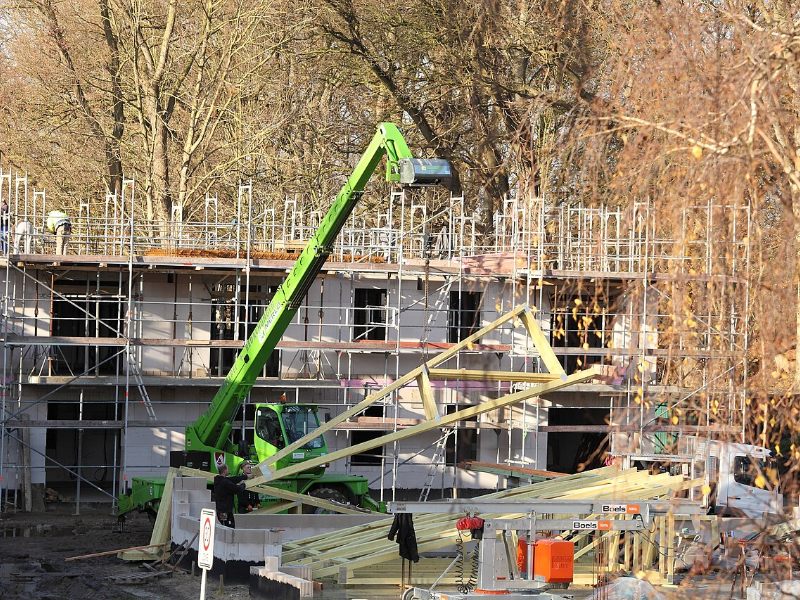 Fermes de charpente hissées par un chariot télescopique sur un bâtiment de logements encore sous échafaudage.