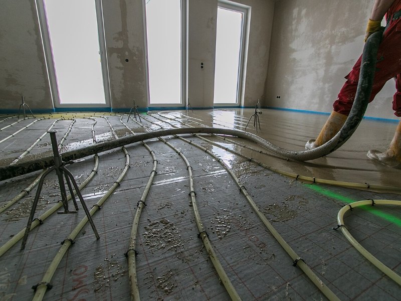 Coulage d’une chape liquide sur un plancher chauffant, dans un logement en travaux dont les menuiseries sont posées.