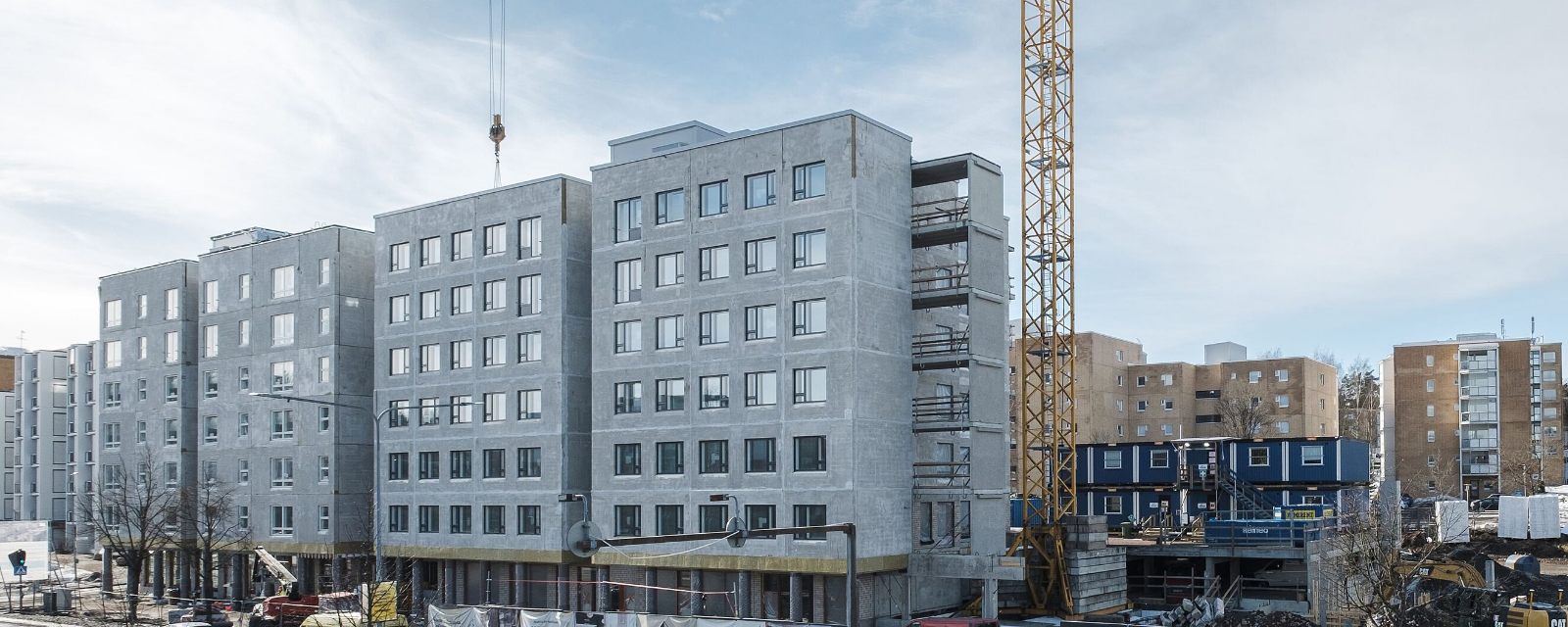 Immeuble de logements de six niveaux en construction, structure béton brut, menuiseries déjà posées et grue à tour sur le chantier.