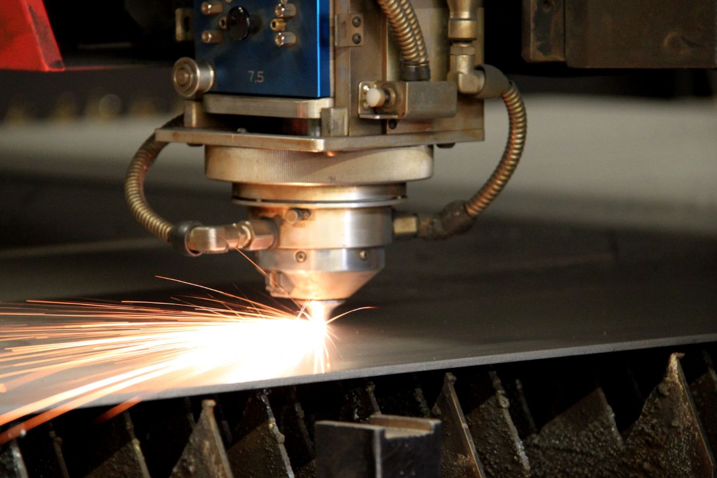 Tête de découpe laser en train de couper une tôle d’acier, gerbe d’étincelles orange le long du trait de coupe.
