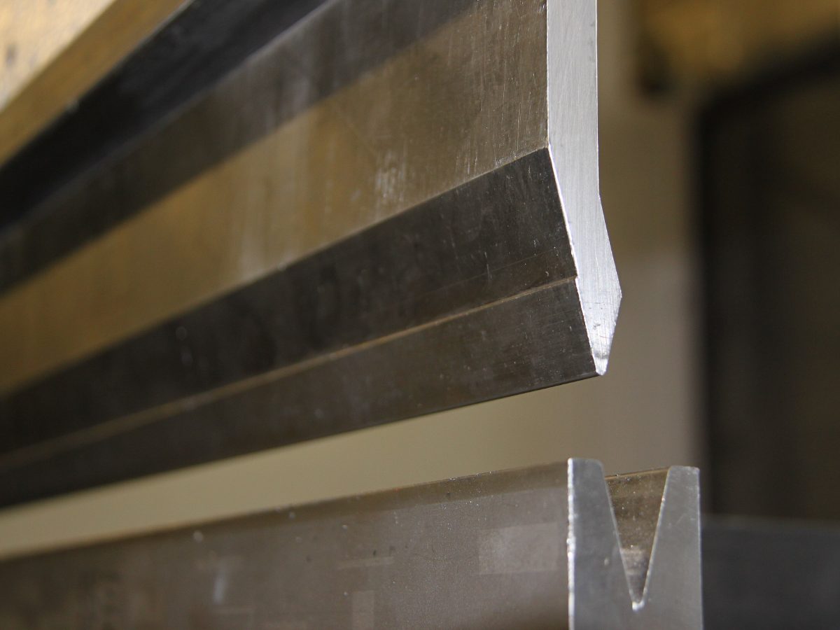 Gros plan du poinçon et de la matrice en V d’une presse plieuse, arêtes vives éclairées par la lumière de l’atelier.