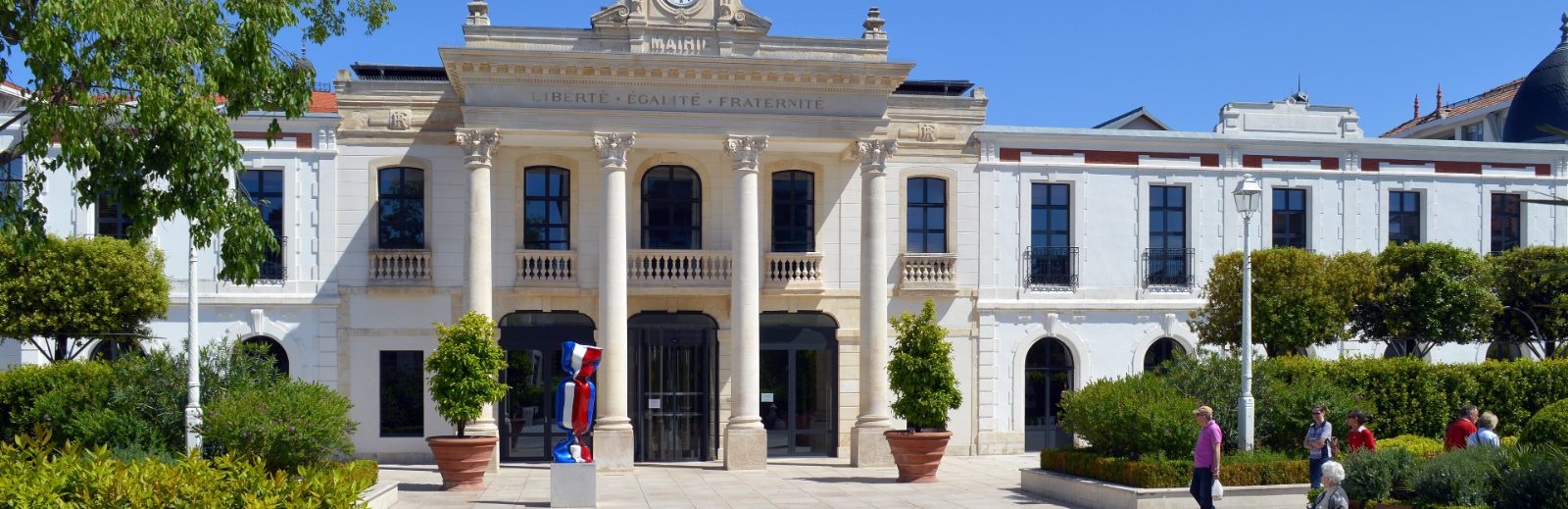Façade de la mairie, colonnade de pierre claire portant l'inscription Liberté Égalité Fraternité, entrée vitrée au centre et jardins de part et d'autre