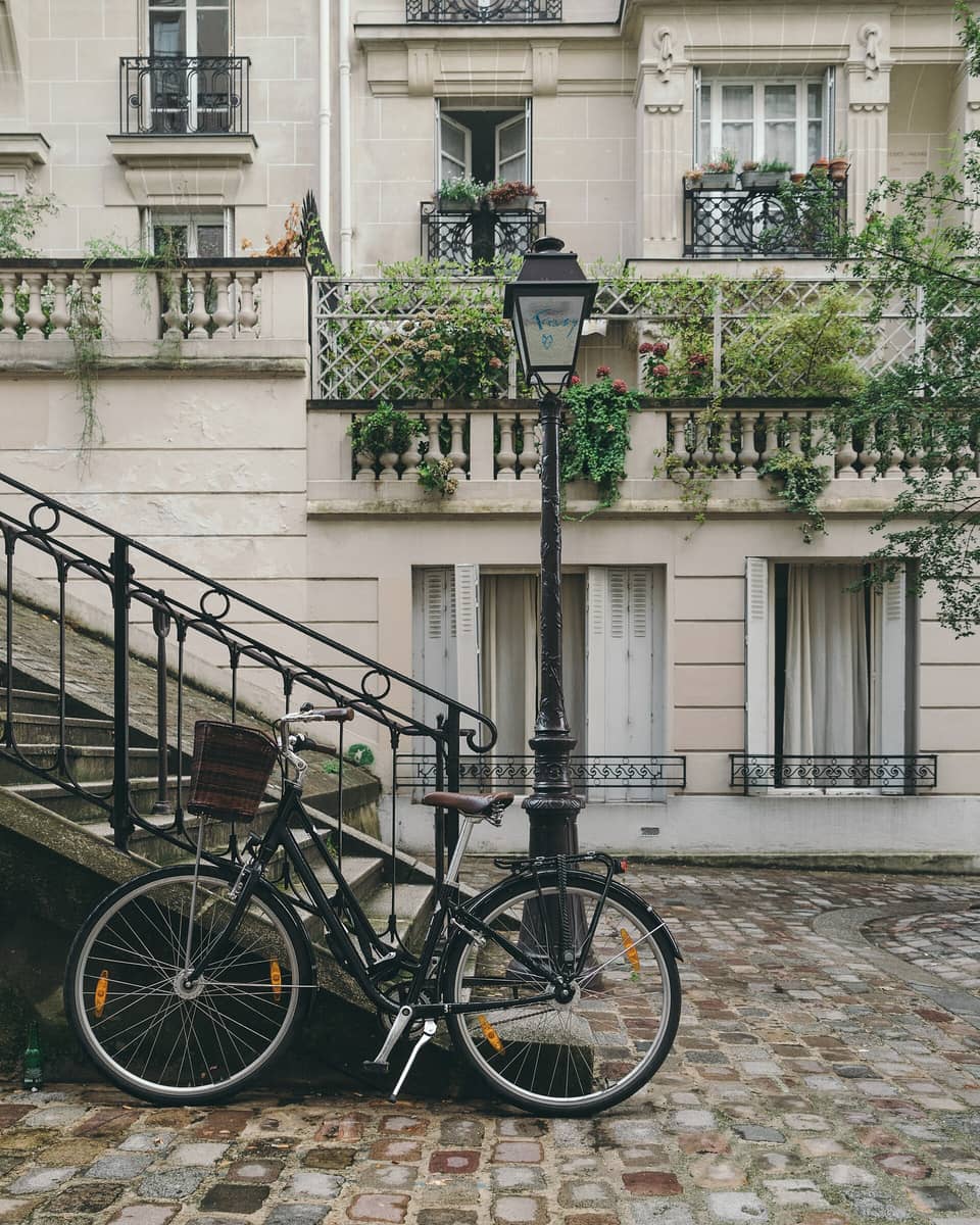 Rue pavée en pente du centre ancien, escalier à rampe de fer, réverbère et façades claires à balcons fleuris