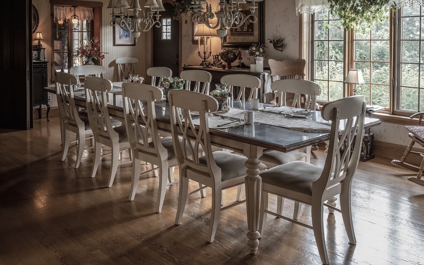 Salle du petit-déjeuner d'une maison ancienne, longue table dressée, chaises claires, parquet et fenêtres sur le jardin