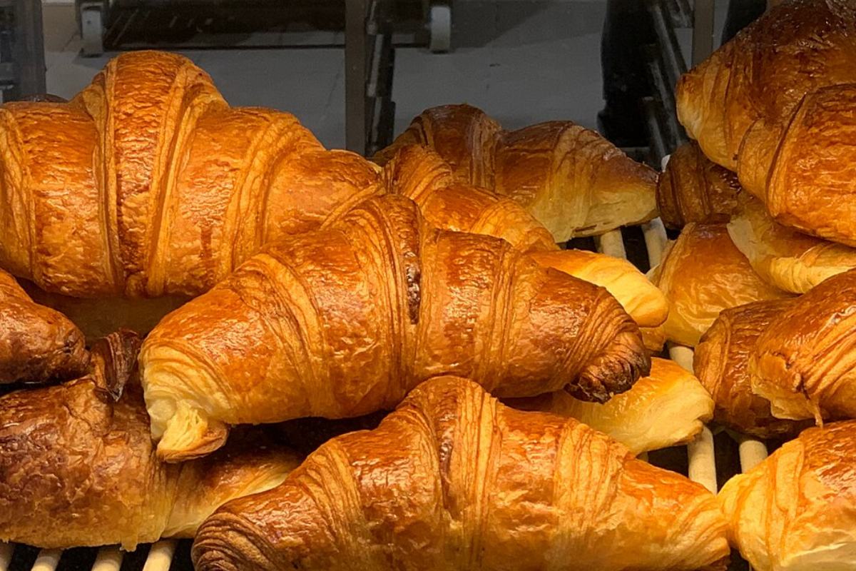 Croissants dorés alignés sur une grille de présentation, ardoise des prix à côté