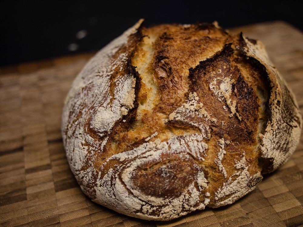 Tourte de meule au levain, croûte farinée et grignée, posée sur une planche
