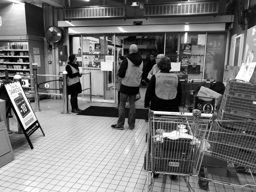 Bénévoles en gilets, de dos, à l'entrée d'un magasin pendant une collecte solidaire