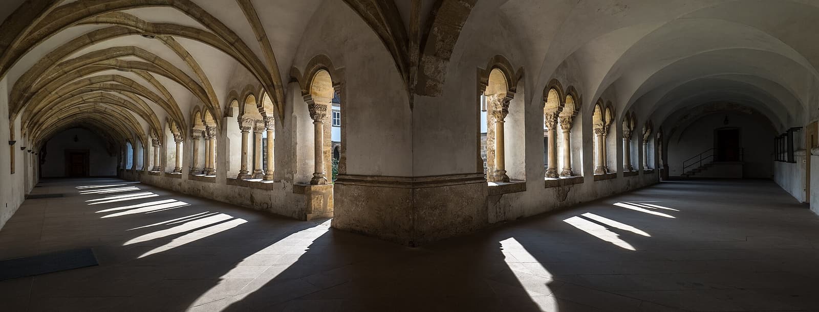 Galerie de pierre voûtée, lumière calme posée sur le sol par les arcades.