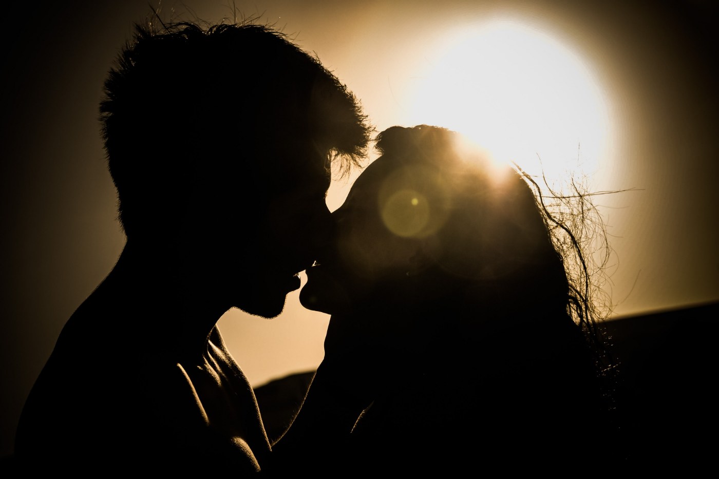 Silhouettes de deux mariés qui s'embrassent devant un soleil bas, halo doré