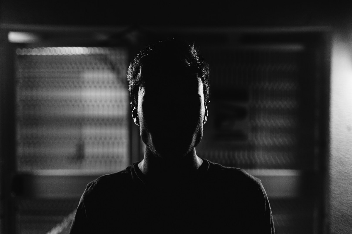 Portrait en noir et blanc, visage entièrement dans l'ombre devant un fond clair strié