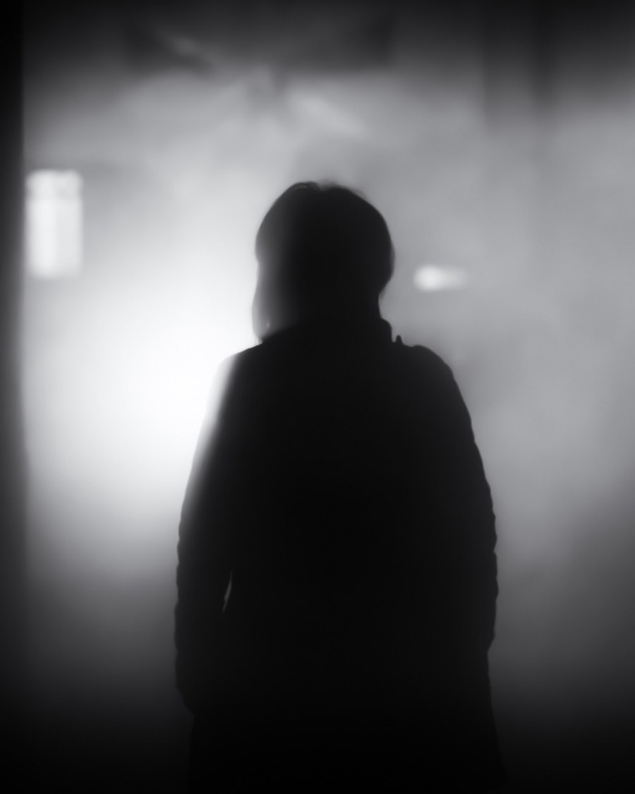 Silhouette sombre d'une personne debout dans une embrasure éclairée, image en noir et blanc