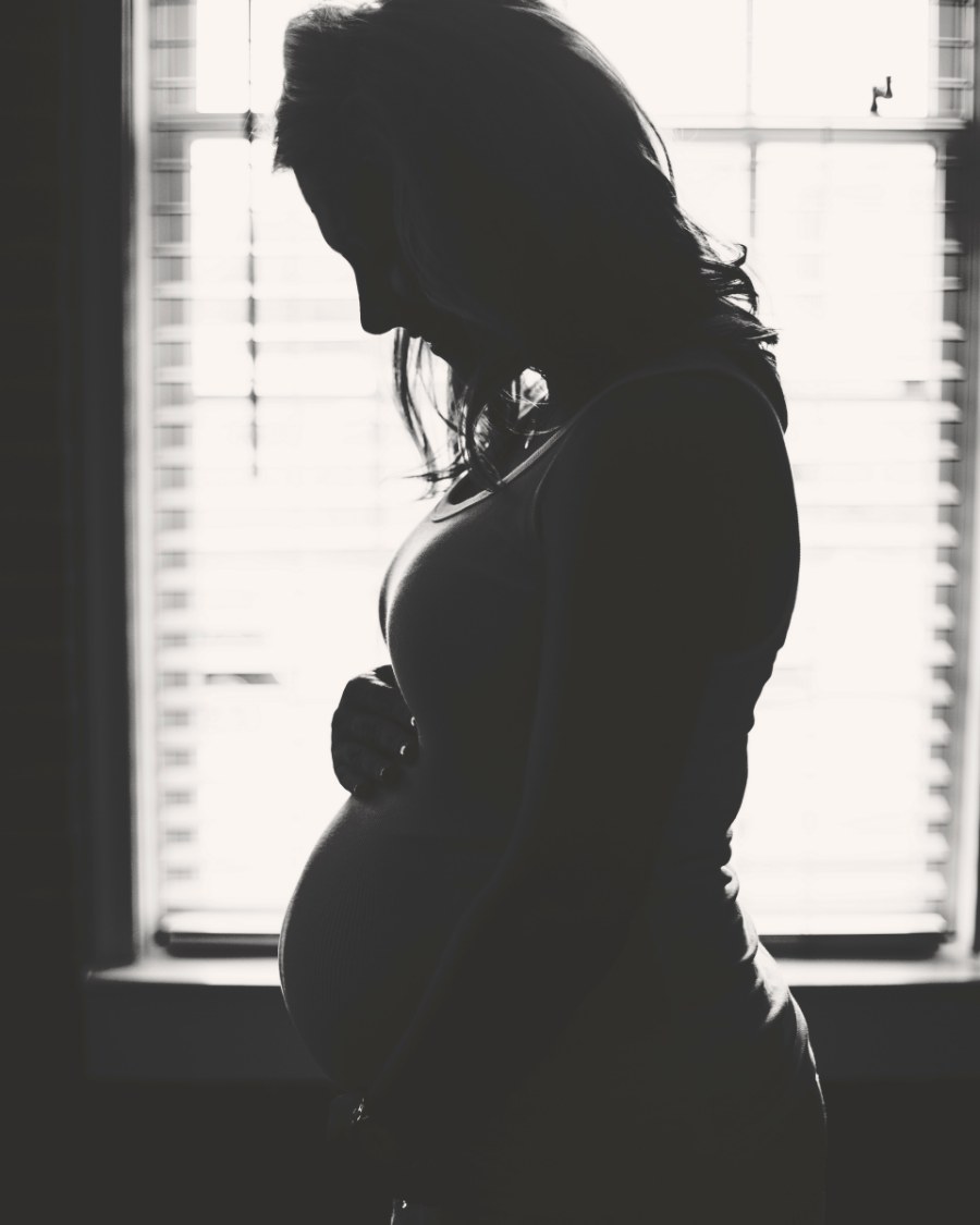 Silhouette de profil d'une femme enceinte devant une fenêtre à stores, noir et blanc
