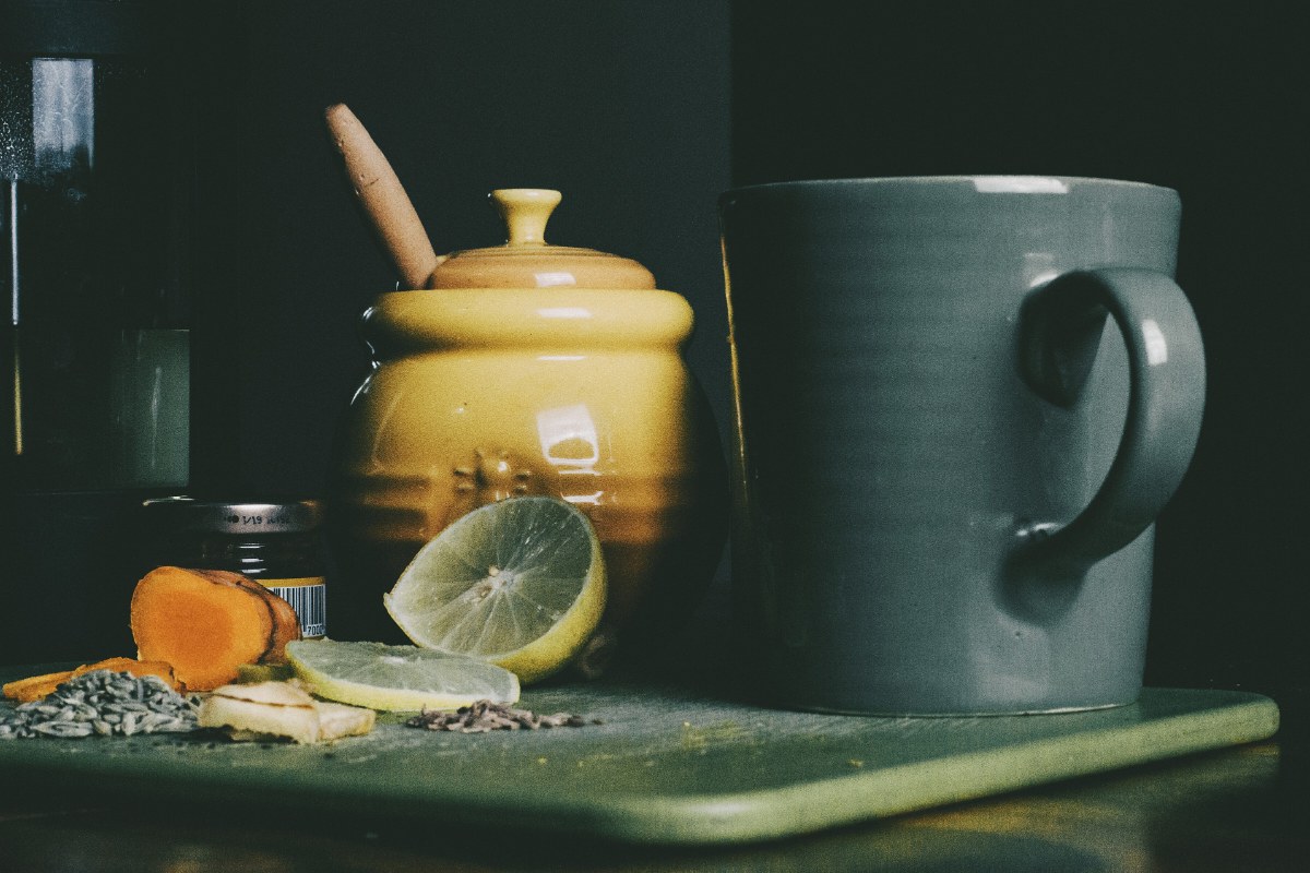 Nature morte sombre, pot en grès jaune, tasse et citron coupé sur une planche