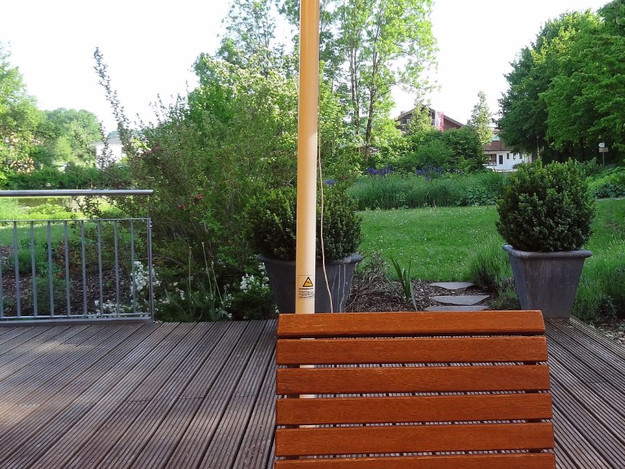 Terrasse en lames de bois exotique prolongée par une pelouse, pas japonais en pierre et arbustes taillés en boule dans des bacs.